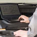 Mechanic using a laptop while looking under the hood of a vehicle to diagnose vehicle issues
