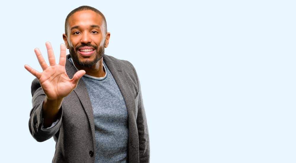 Man in a grey blazer leaning forward with five fingers up
