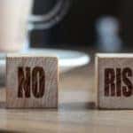 Two wooden blocks that say "NO RISK" on them sitting on a table in front of a clear mug on a white plate