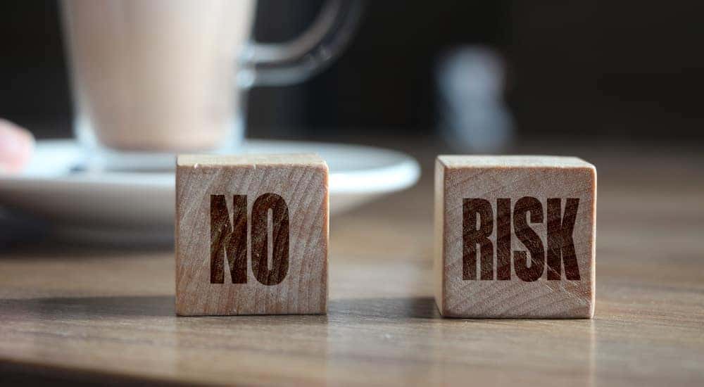 Two wooden blocks that say "NO RISK" on them sitting on a table in front of a clear mug on a white plate