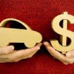 Woman in a red sweater holding a brown wooden car in one hand and a brown wooden dollar sign in the other
