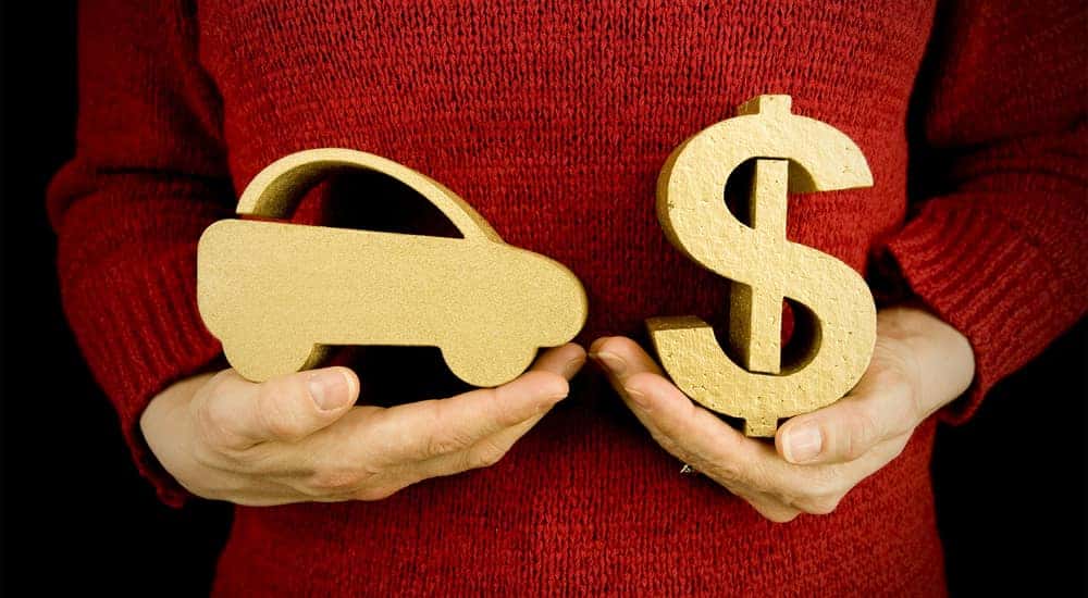 Woman in a red sweater holding a brown wooden car in one hand and a brown wooden dollar sign in the other