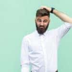 Man in a white button-up shirt scratching his head in front of a green wall