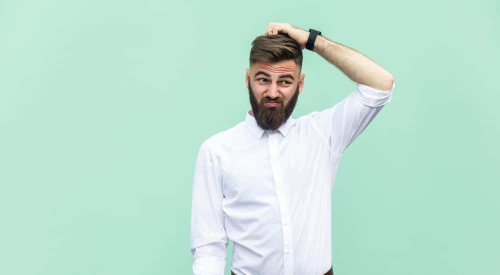 Man in a white button-up shirt scratching his head in front of a green wall