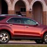 Red 2011 Chevrolet Equinox SUV parked in the driveway of a large brick building