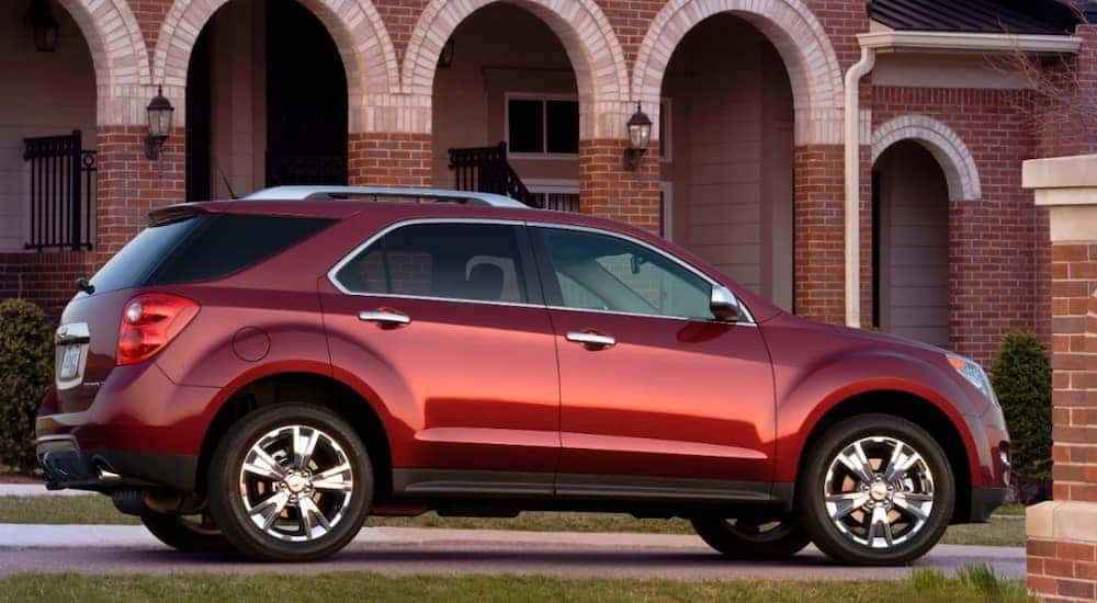Red 2011 Chevrolet Equinox SUV parked in the driveway of a large brick building