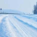 Snow covered road with tire tracks down the middle in front of a tall snowy mountain