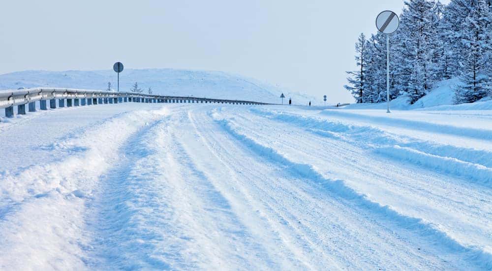 Snow covered road with tire tracks down the middle in front of a tall snowy mountain
