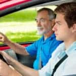 Teen boy in a blue shirt driving a red car with his dad in the passenger seat