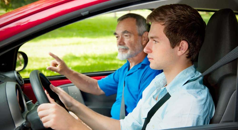 Teen boy in a blue shirt driving a red car with his dad in the passenger seat