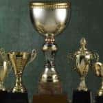 Seven gold trophies sitting next to one another in front of a green wall