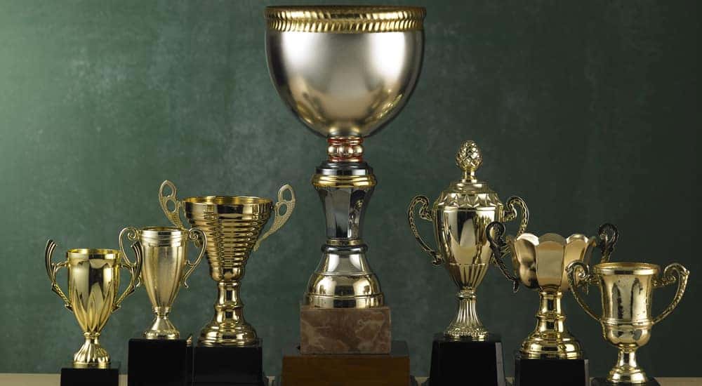 Seven gold trophies sitting next to one another in front of a green wall