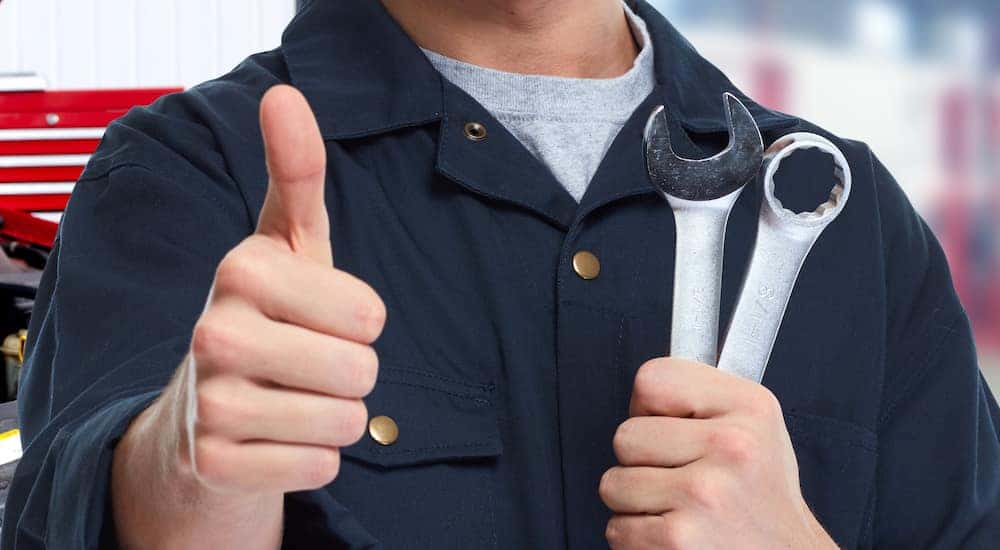Auto service mechanic holding wrenches in one hand and giving a thumbs up with the other
