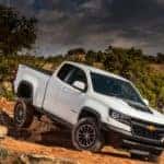 White 2017 Chevrolet Colorado pickup truck driving down rocky dirt terrain
