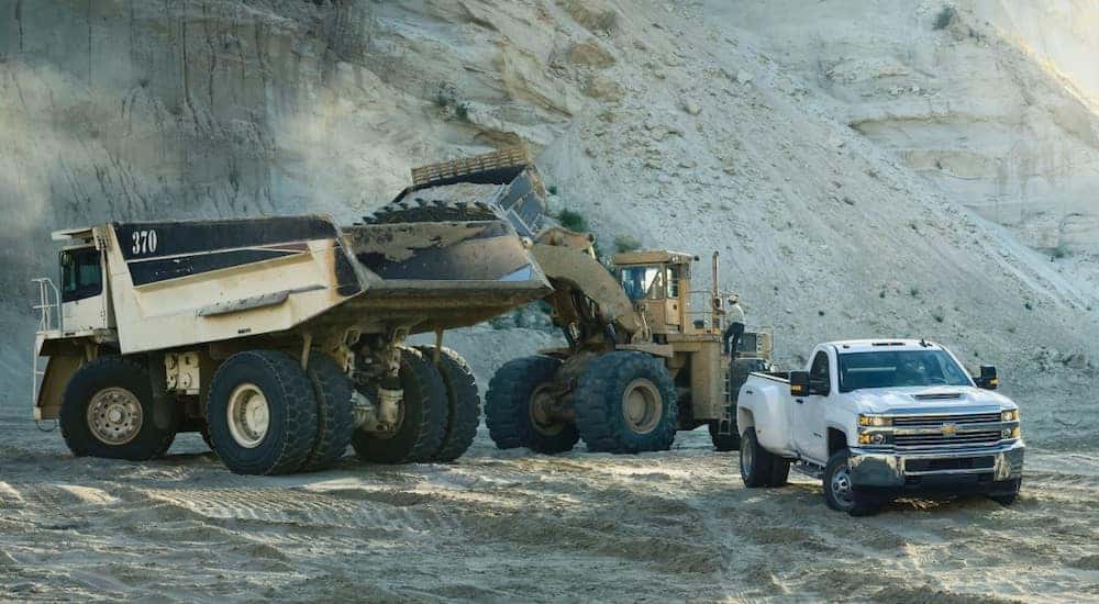 White 2017 Silverado 3500HD pickup truck parked in front of construction vehicles and a tall pile of sand