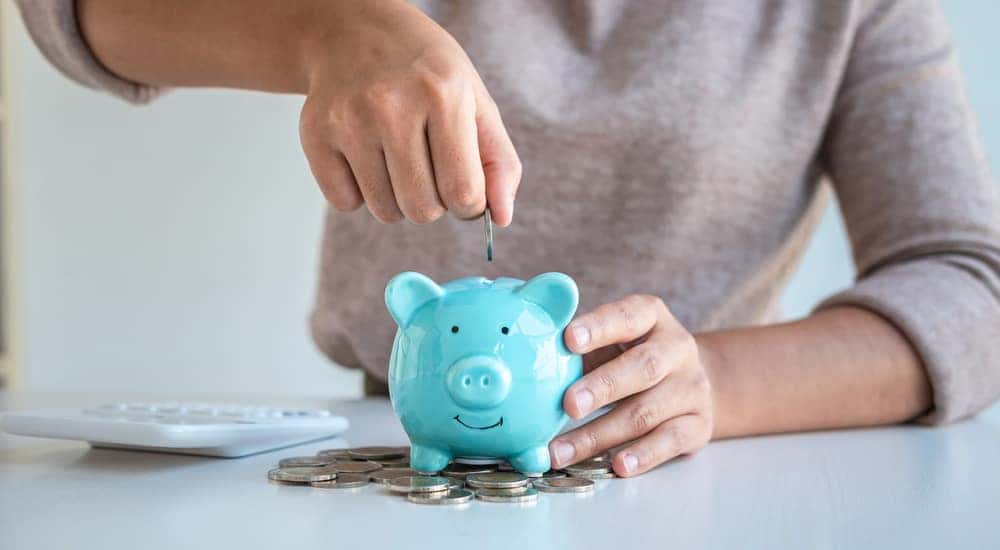 Hand placing change into a blue piggybank that is sitting on top of a pile of change