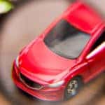 Magnifying glass showing a close-up of a red toy car that is sitting on a brown table next to two other toy cars