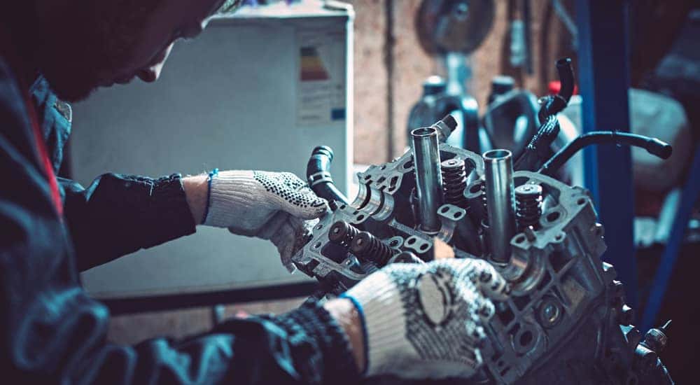 Mechanic in a black jacket and white gloves holding onto and inspecting an engine