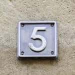 Silver plaque with the number five on it against a tan cement background
