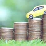 Yellow toy car driving down progressively shorter stacks of coins in the grass
