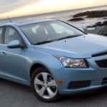 Baby blue 2011 Chevrolet Cruze parked on pavement in font of rocky water