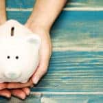 Hands holding a white piggybank on top of a blue wooden table