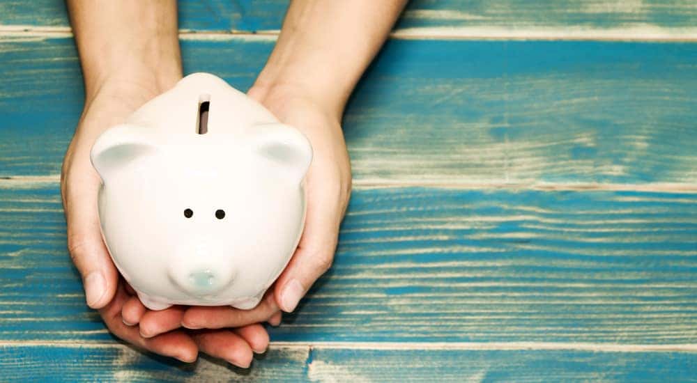 Hands holding a white piggybank on top of a blue wooden table