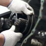 Hands in white gloves performing maintenance on a vehicle's transmission