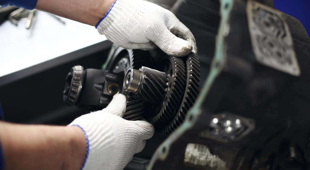 Hands in white gloves performing maintenance on a vehicle's transmission