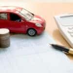 Red toy car, coins, a paper bill, pen, and a calculator on a brown desk
