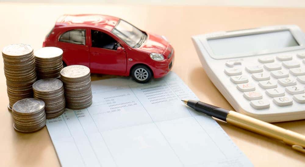 Red toy car, coins, a paper bill, pen, and a calculator on a brown desk