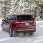 Maroon 2018 Chevrolet Traverse driving down a snowy road next to snowy trees