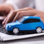 Hands typing on the keyboard of a silver laptop with a blue toy car sitting on it