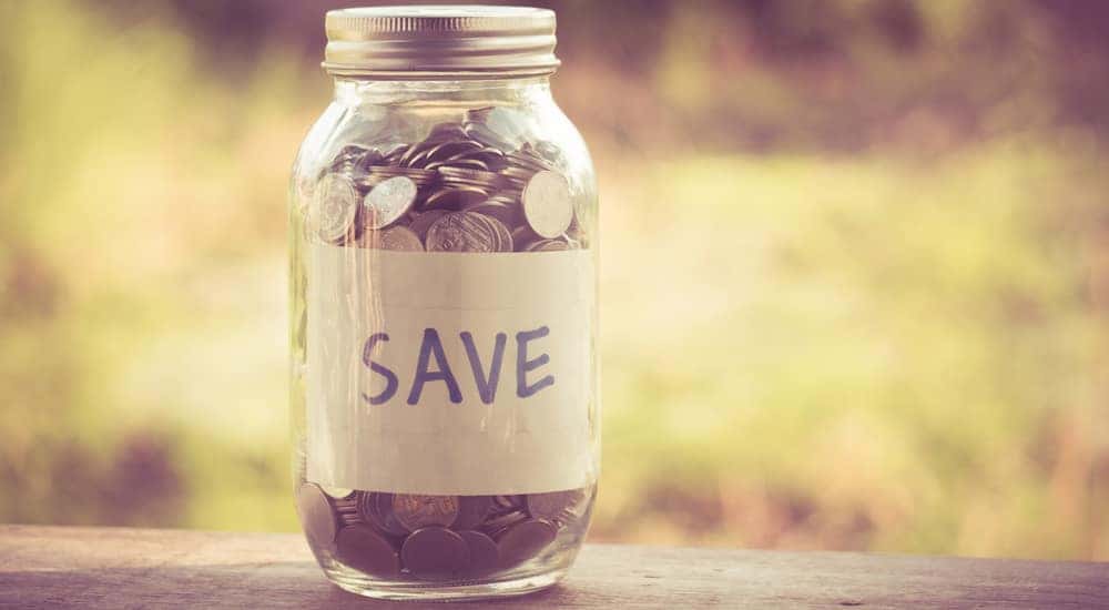 Mason jar full of coins with the word "SAVE" on it sitting on a brown ledge