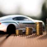 White toy sports vehicle on a brown table next to four consecutively taller stacks of coins