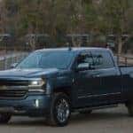 Blue 2017 Chevrolet Silverado pickup truck parked on a dirt path between fences with horses behind them