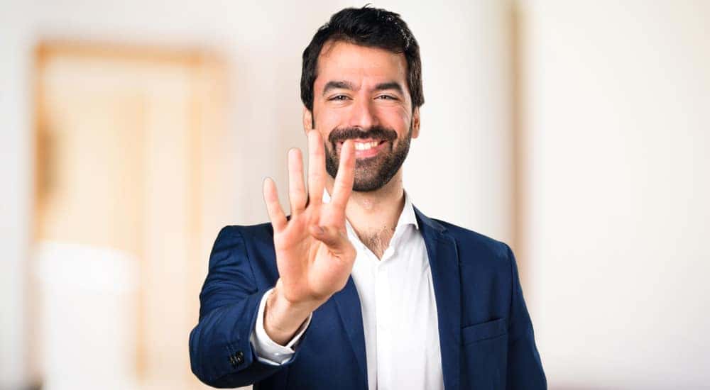 Man with facial hair in a suit holding three fingers up and smiling
