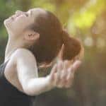 Woman calming her nerves with her arms out and taking a deep breath in front of trees