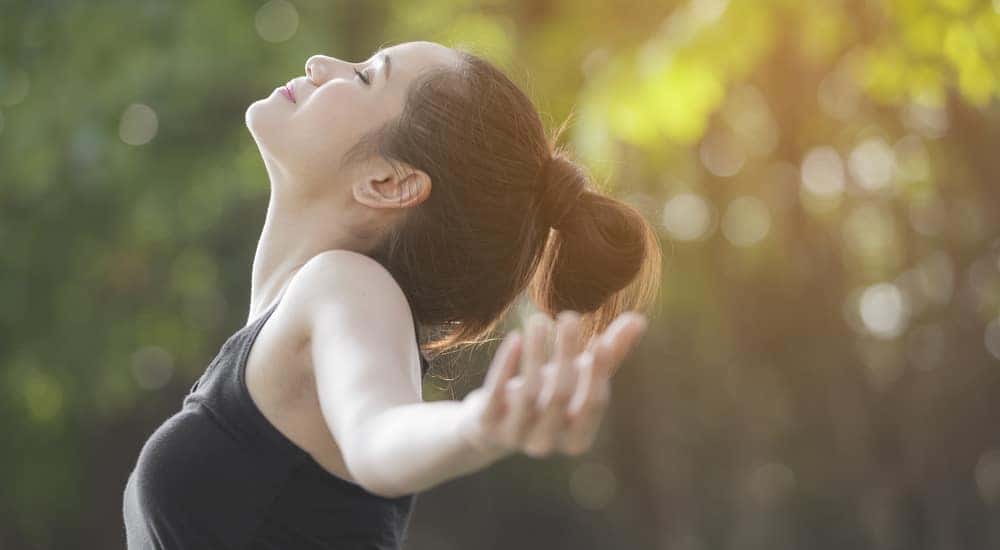 Woman calming her nerves with her arms out and taking a deep breath in front of trees