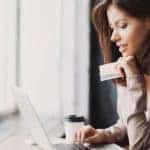 Woman sitting at a desk and using a laptop while holding a credit card