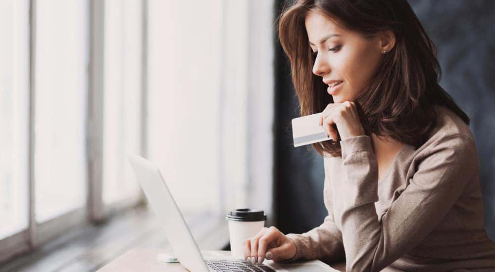 Woman sitting at a desk and using a laptop while holding a credit card