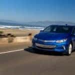 Blue 2017 Chevrolet Volt driving down a paved road with mountains in the distance