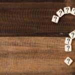 White tiles with question marks on them formed into the shape of a larger question mark on a wooden table