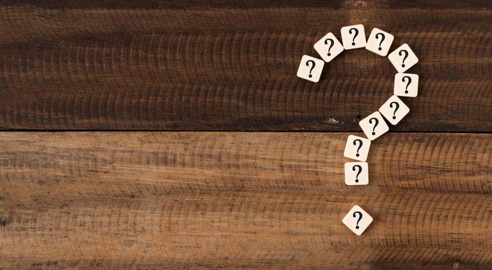 White tiles with question marks on them formed into the shape of a larger question mark on a wooden table