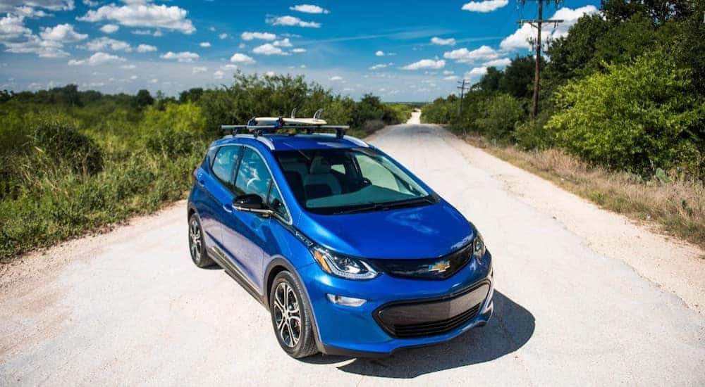 Blue 2017 Chevrolet Bolt EV parked diagonally across a dirt road with trees and plants on both sides