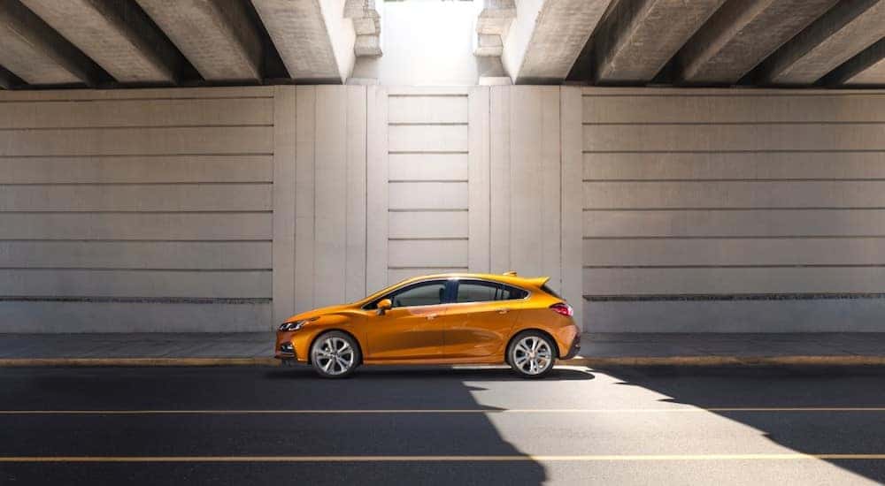 Orange 2017 Chevrolet Cruze hatchback driving under a bridge with the sun peeking through