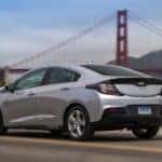 Silver 2017 Chevrolet Volt driving down a paved road past a tall, orange bridge