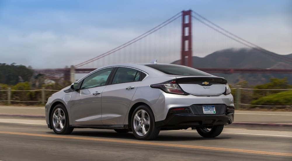 Silver 2017 Chevrolet Volt driving down a paved road past a tall, orange bridge