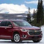 Maroon 2018 Chevrolet Traverse SUV parked on a snowy road in front of tall, snowy mountains