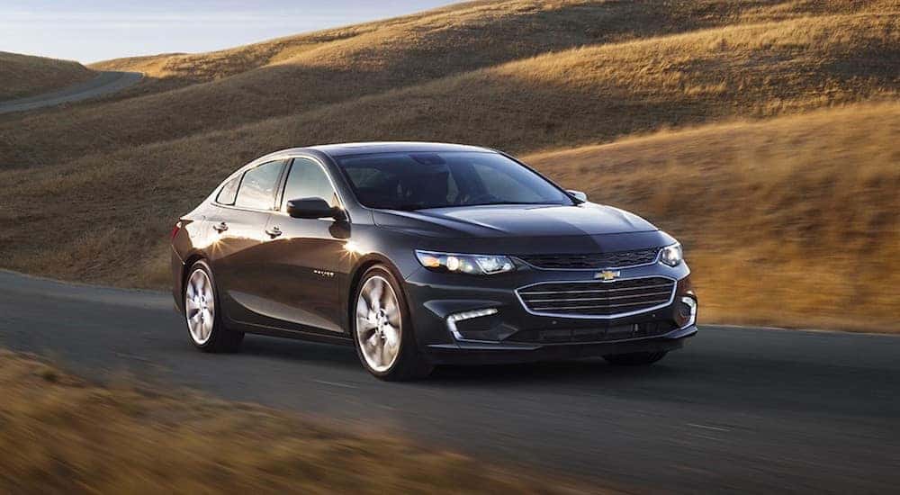 Black 2017 Chevrolet Malibu sedan driving down a paved path past brown, grassy hills